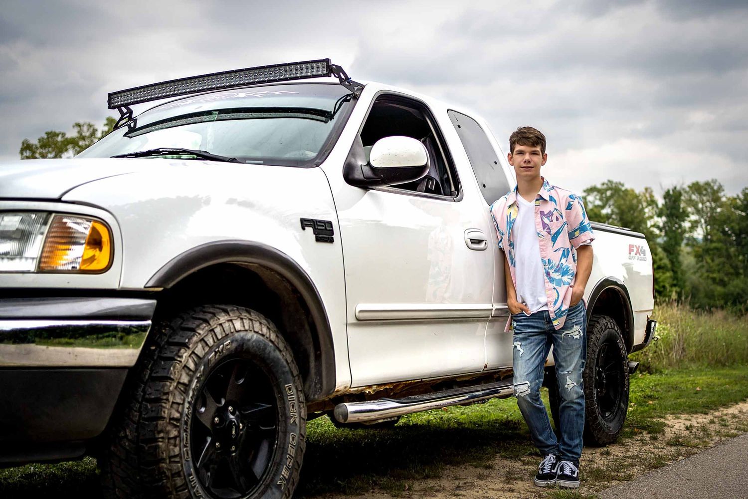 A white Ford F150 pickup truck is photographed from multiple angles on a dirt road with dramatic cloudy skies.
