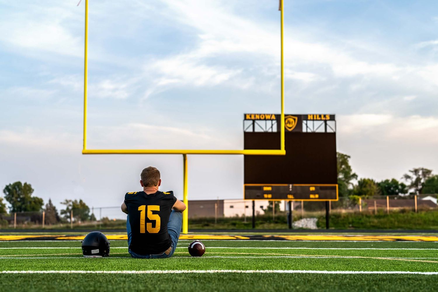 Football field with yellow goal posts and scoreboard against a cloudy sky at sunset.