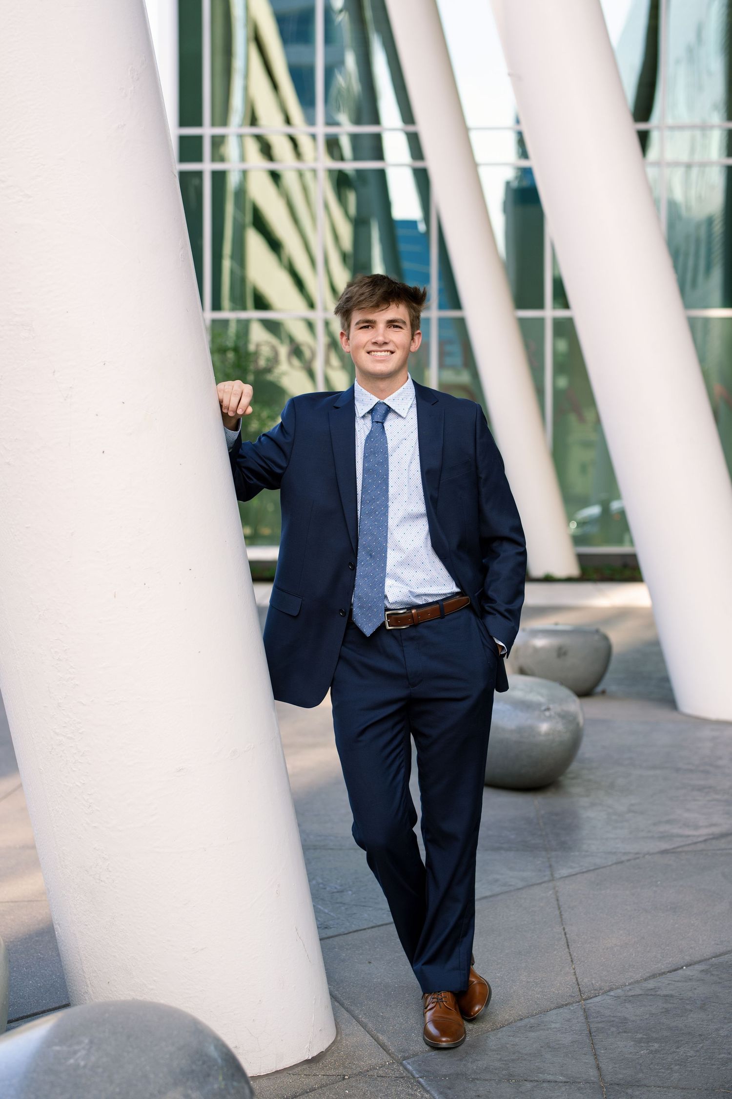Professional in a navy suit poses playfully between white architectural columns in an urban setting.