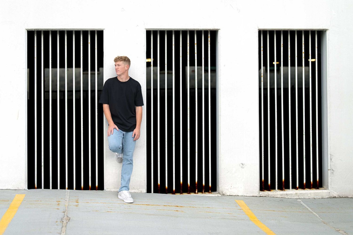 A person in a black t-shirt and jeans stands against a white wall with black vertical stripes in a modern setting.