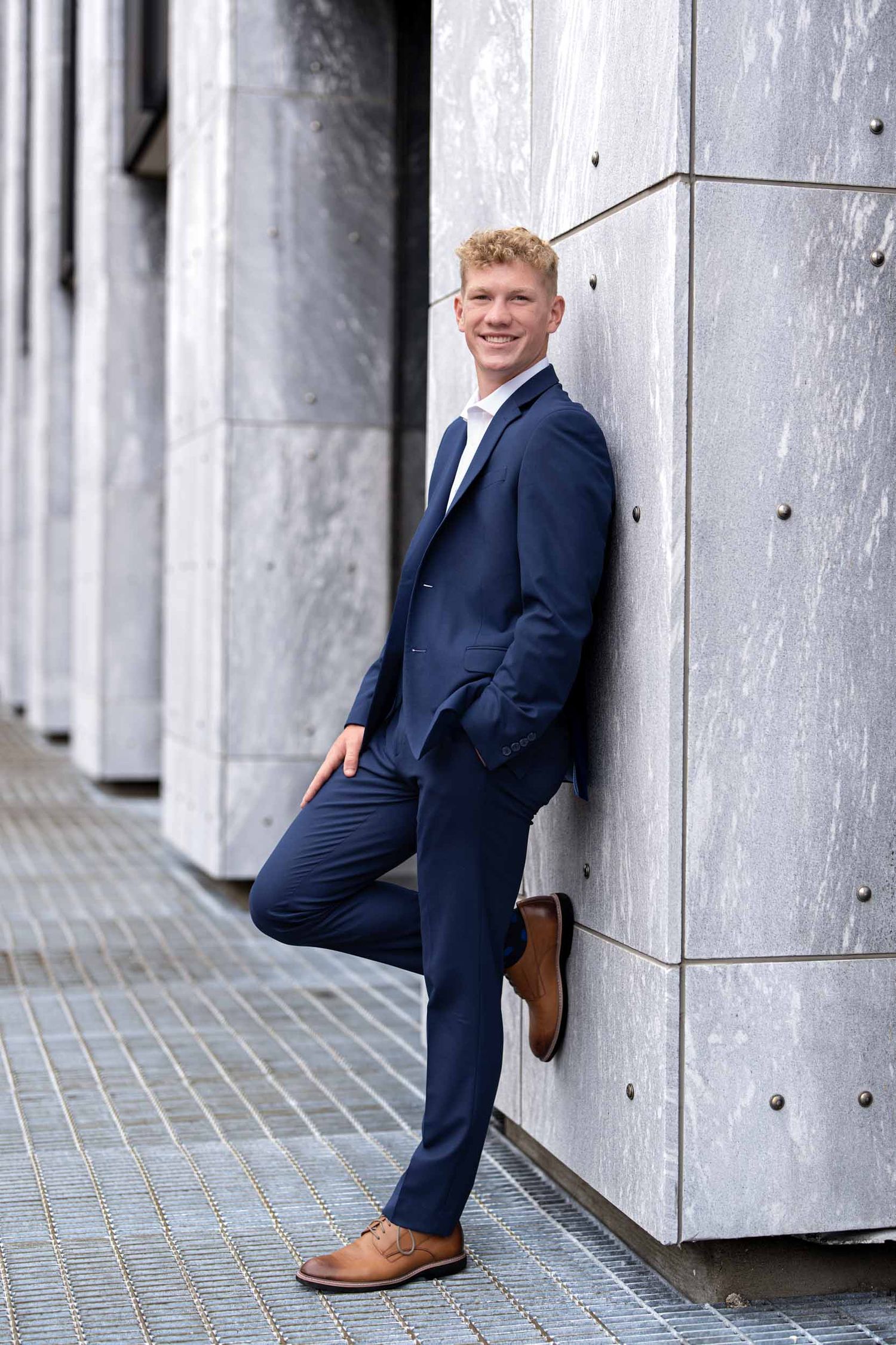 Professional portrait series showing different poses against a modern architectural backdrop in a navy suit.