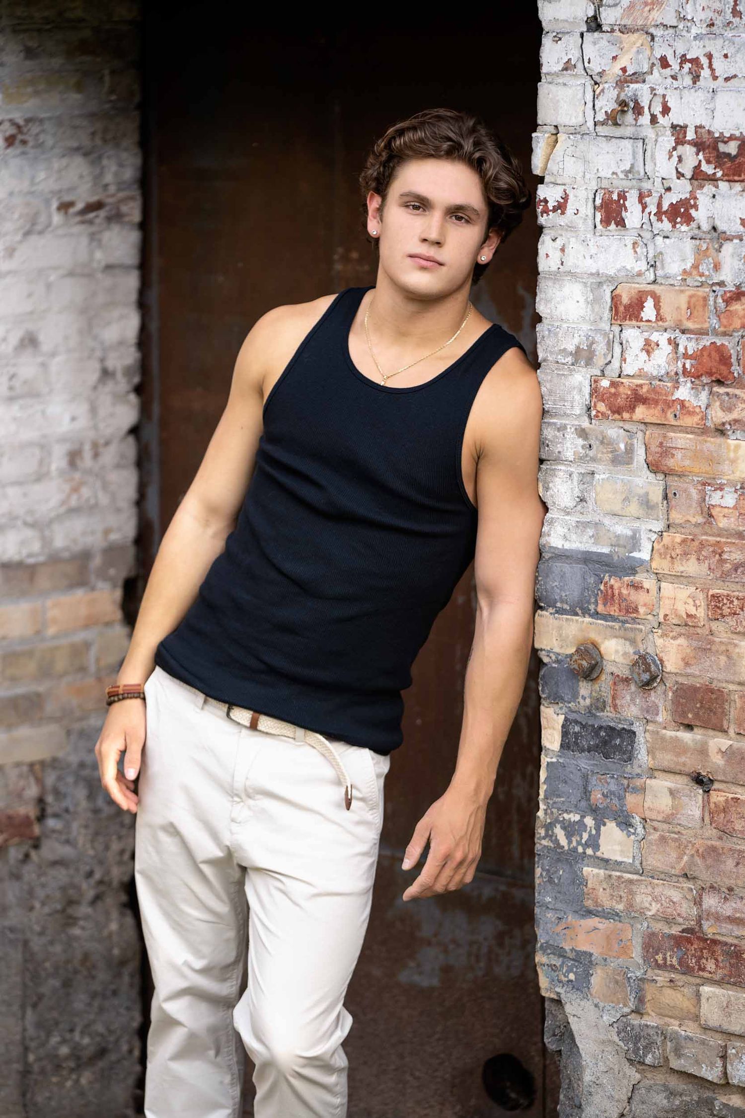 Casual fashion photo series against rustic brick wall showing black tank top and white pants in multiple poses.