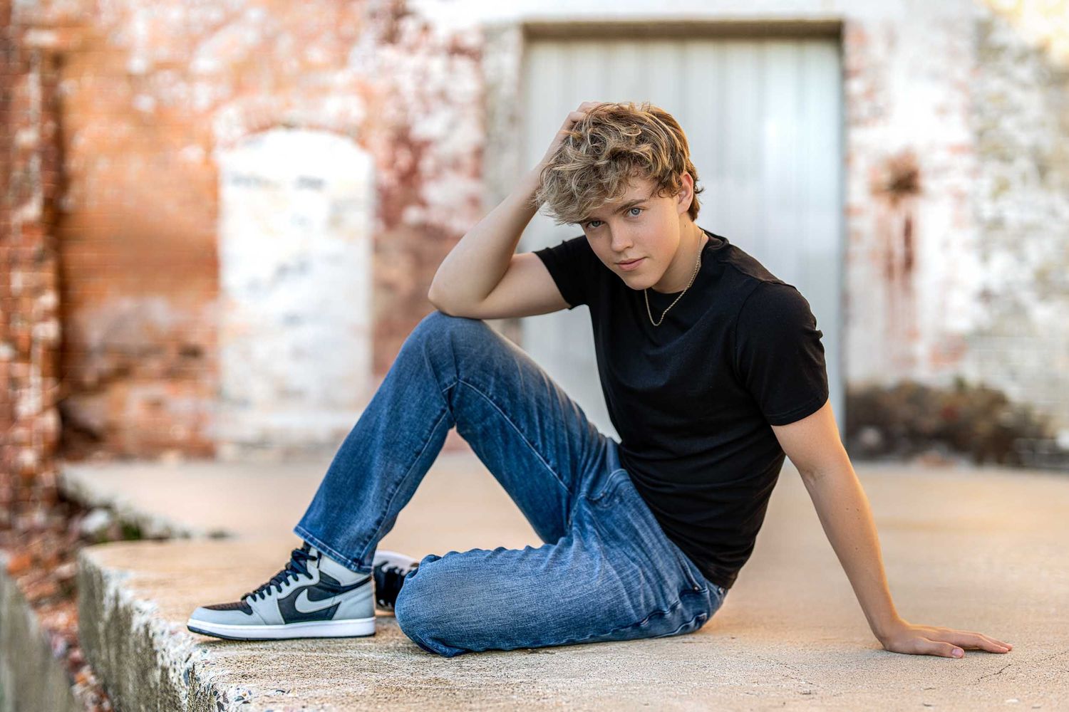 A person in jeans and black t-shirt poses in various casual positions against a rustic brick wall background.
