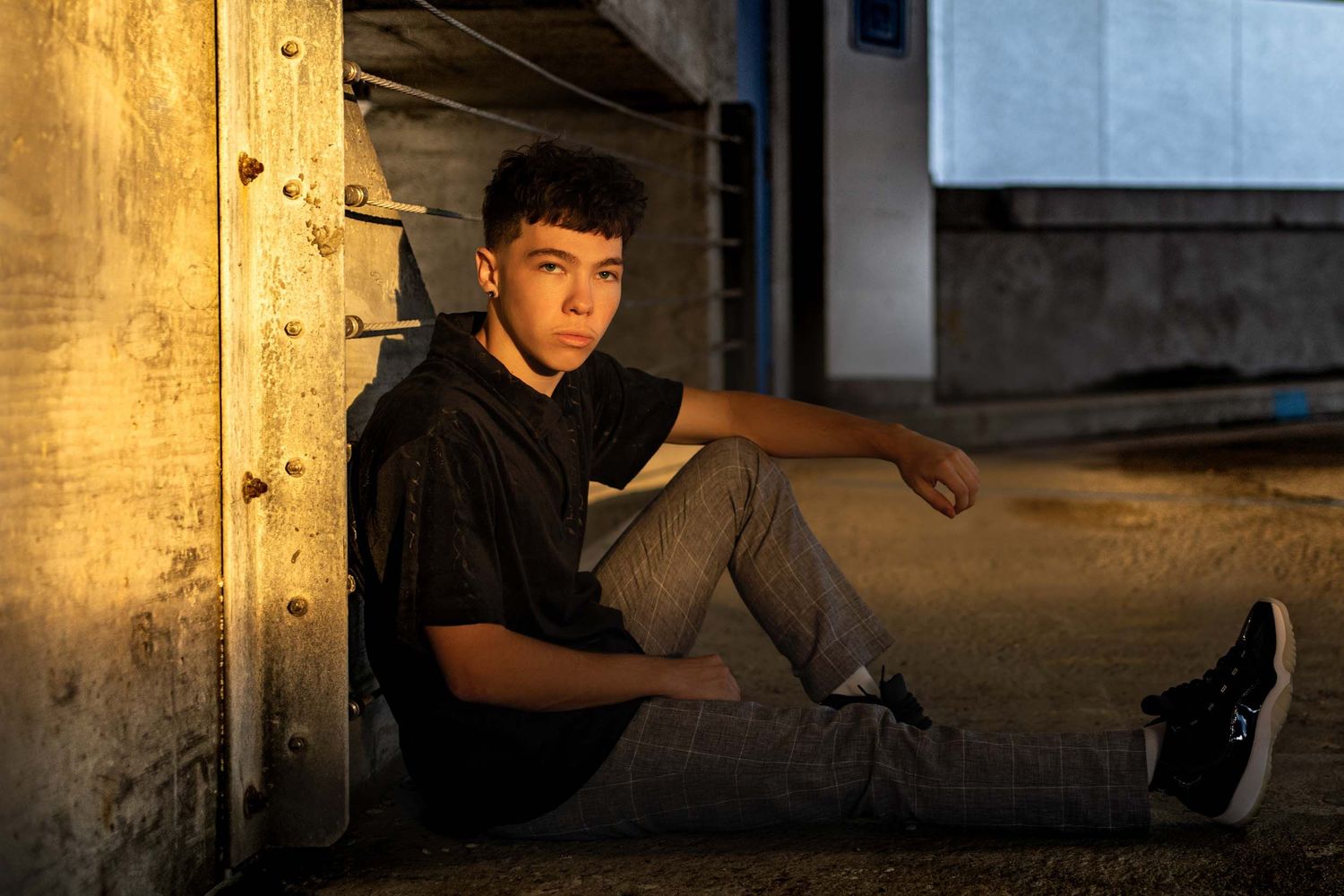 A young person performs a skateboarding trick at sunset in an urban setting with dramatic lighting and shadows.