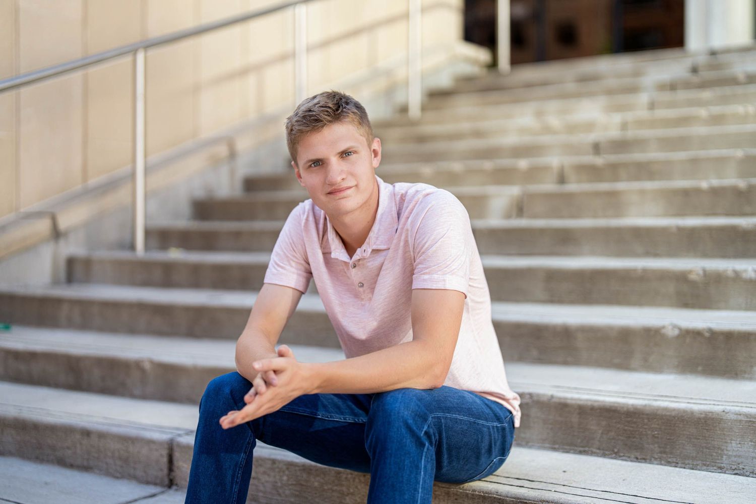 A person in a pink t-shirt and jeans sits thoughtfully on concrete steps in an urban setting.