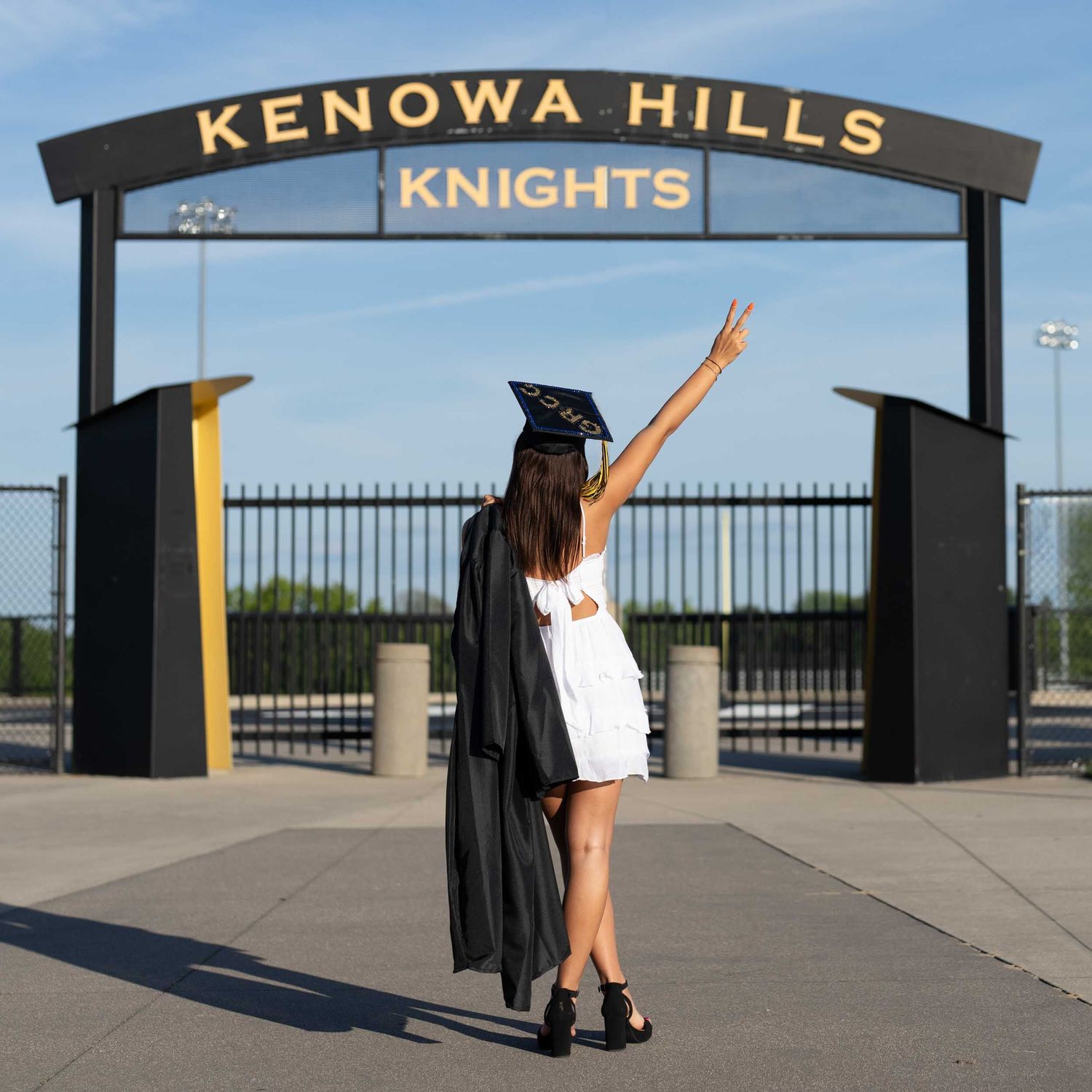 Graduate in cap and gown poses for celebratory photos in front of Kenosha Hills Knights entrance gate.