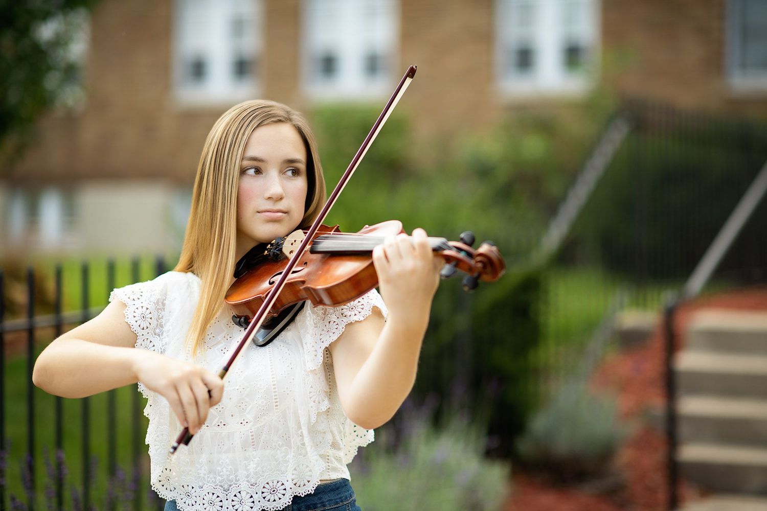 Musician playing violin outdoors in a white lace dress against a natural backdrop.