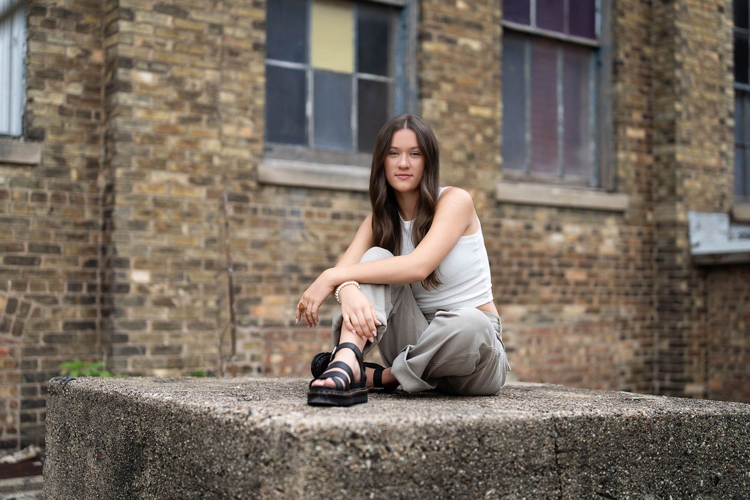 A person in casual attire sits on a concrete ledge against a brick building backdrop.