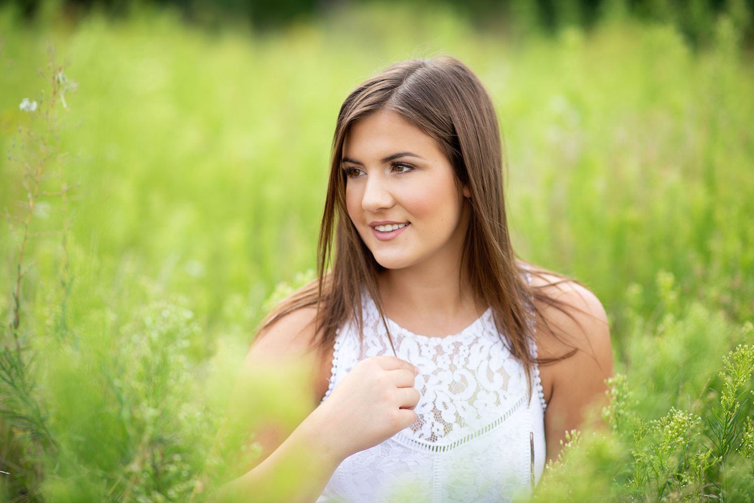 Young brunette woman in white lace top smiling outdoors in lush green field on a sunny day.