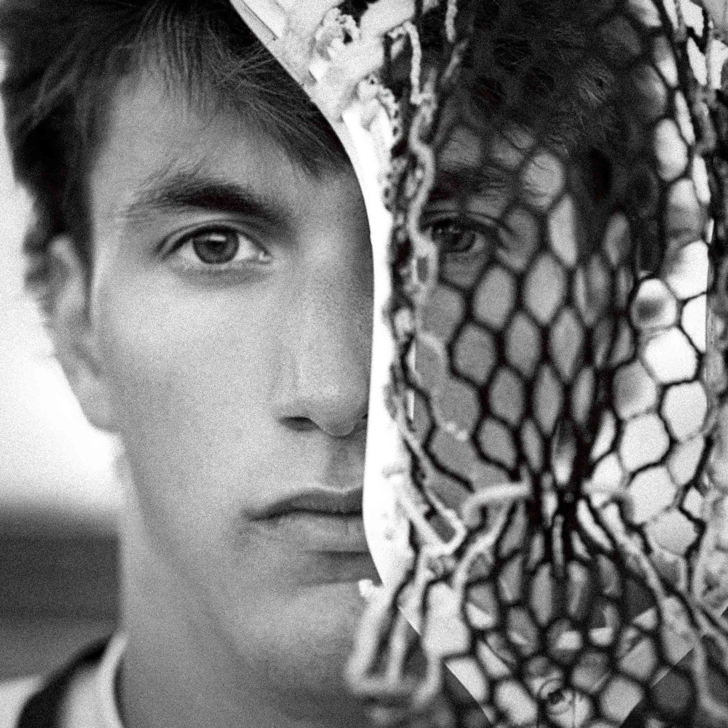 Artistic black and white close-up portrait with chain link fence creating dramatic shadow effect.