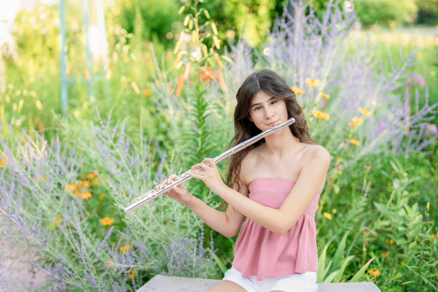 A musician plays flute outdoors among blooming flowers and lavender.