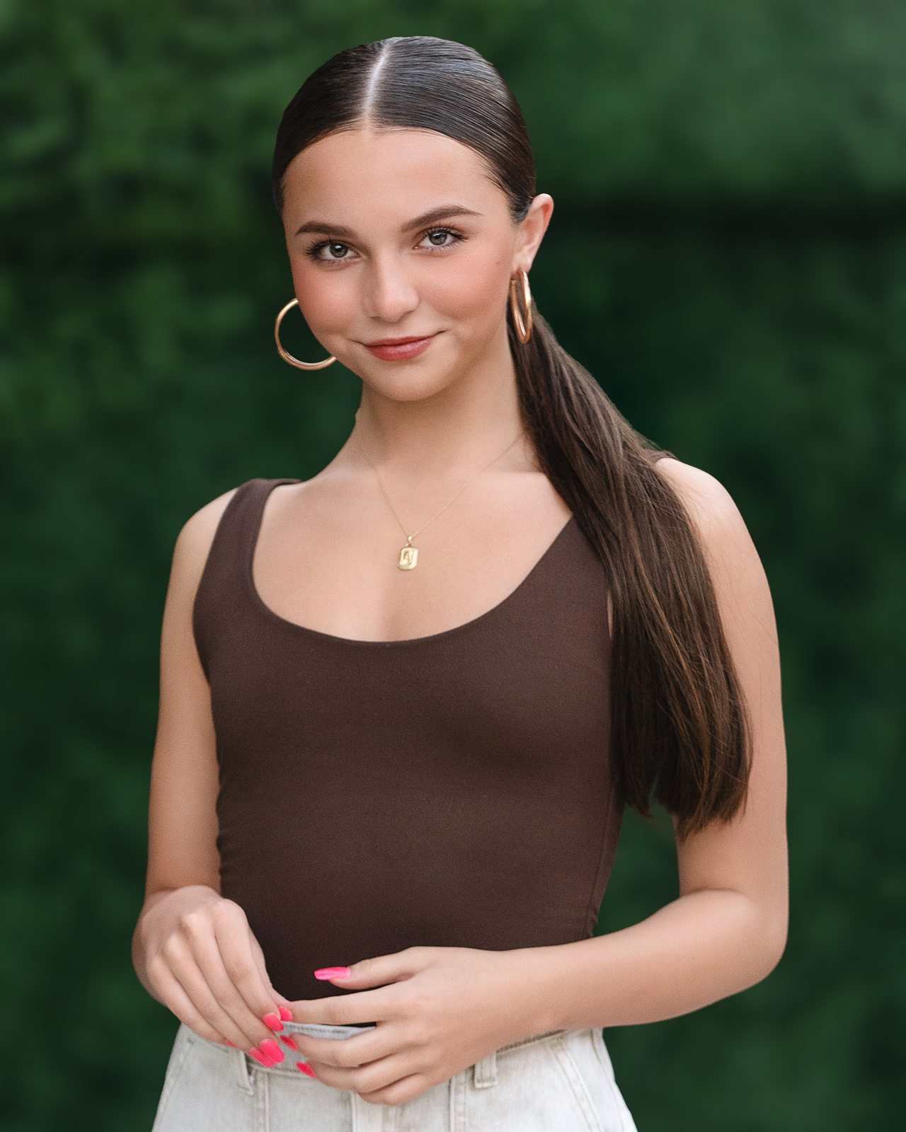 Young woman in brown tank top with gold hoop earrings and necklace, long dark hair, pink nails, green background.
