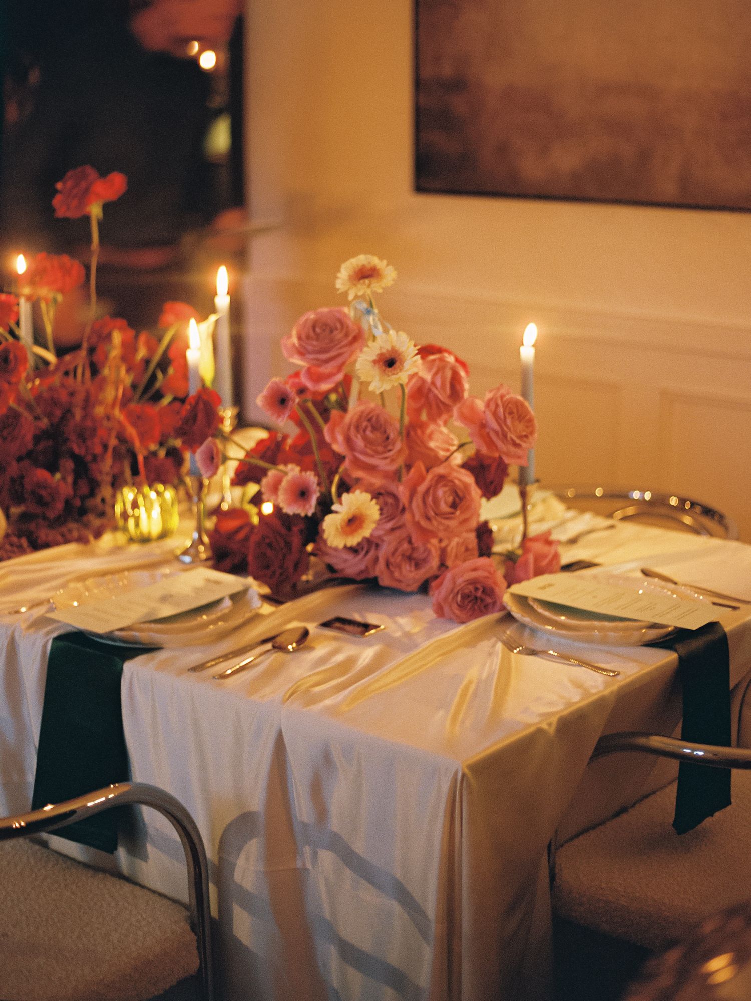 Elegant candlelit table with pink roses centerpiece, white linen, and gold cutlery for a romantic dinner setting.