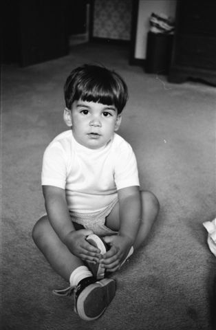A series of black and white photos showing a small child sitting on carpet while playing with their shoes.