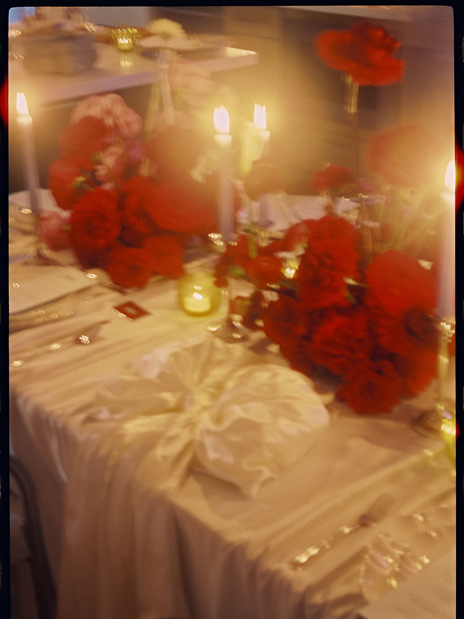 Elegant wedding reception table with red floral centerpieces, white linen, and glowing candles creating a romantic ambiance.