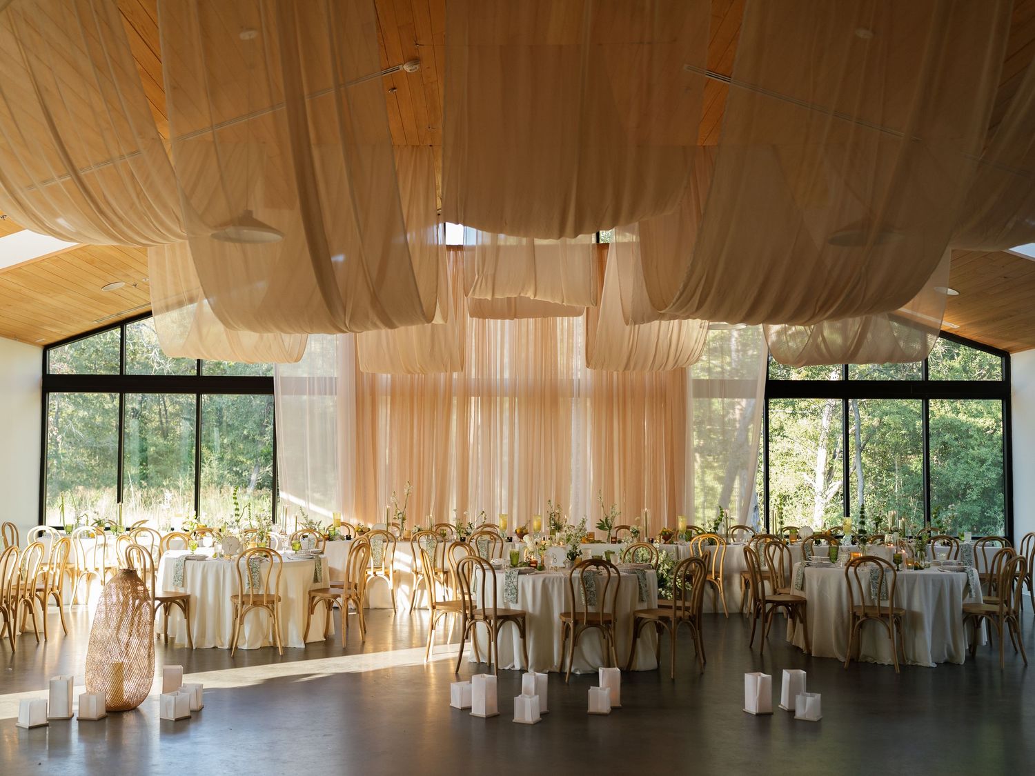 Panoramic view of an elegant wedding reception venue with white drapes, wooden ceiling beams, and natural light.