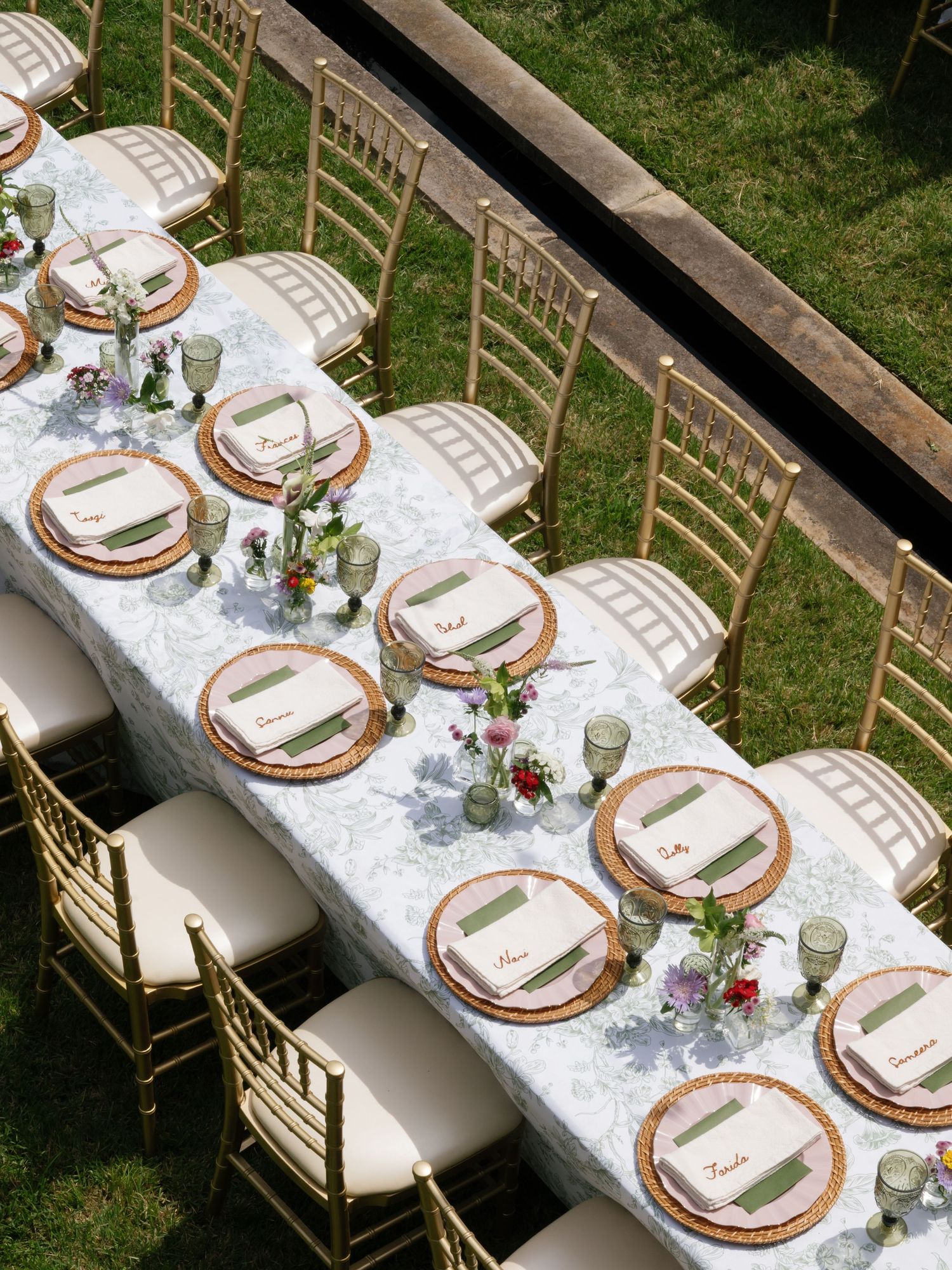 Elegant outdoor wedding reception table with gold chiavari chairs, marble linens, copper chargers, and floral centerpieces.