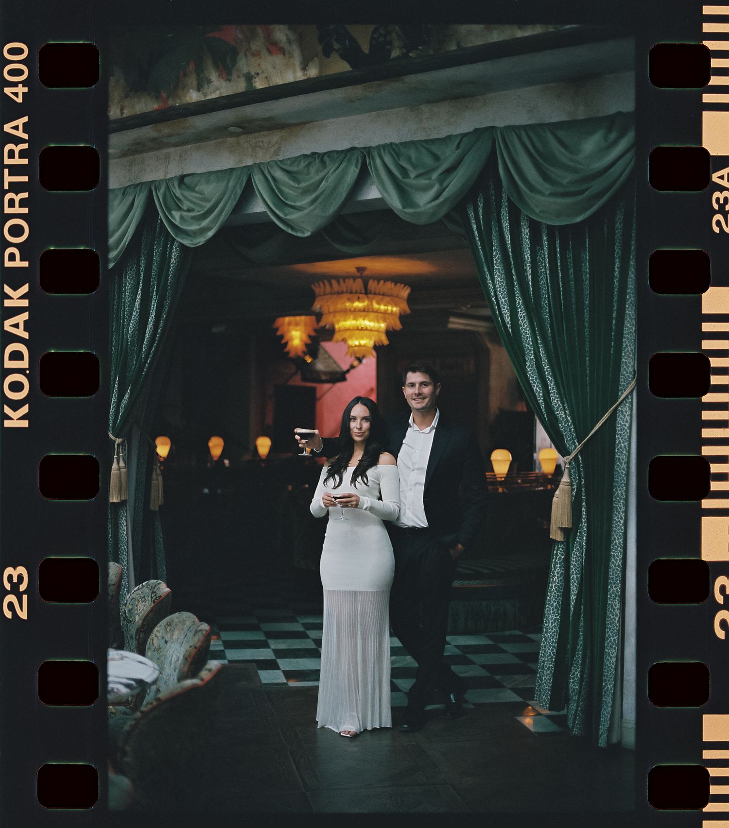 A couple poses in an elegant venue with emerald green curtains and warm lighting creating a romantic atmosphere.
