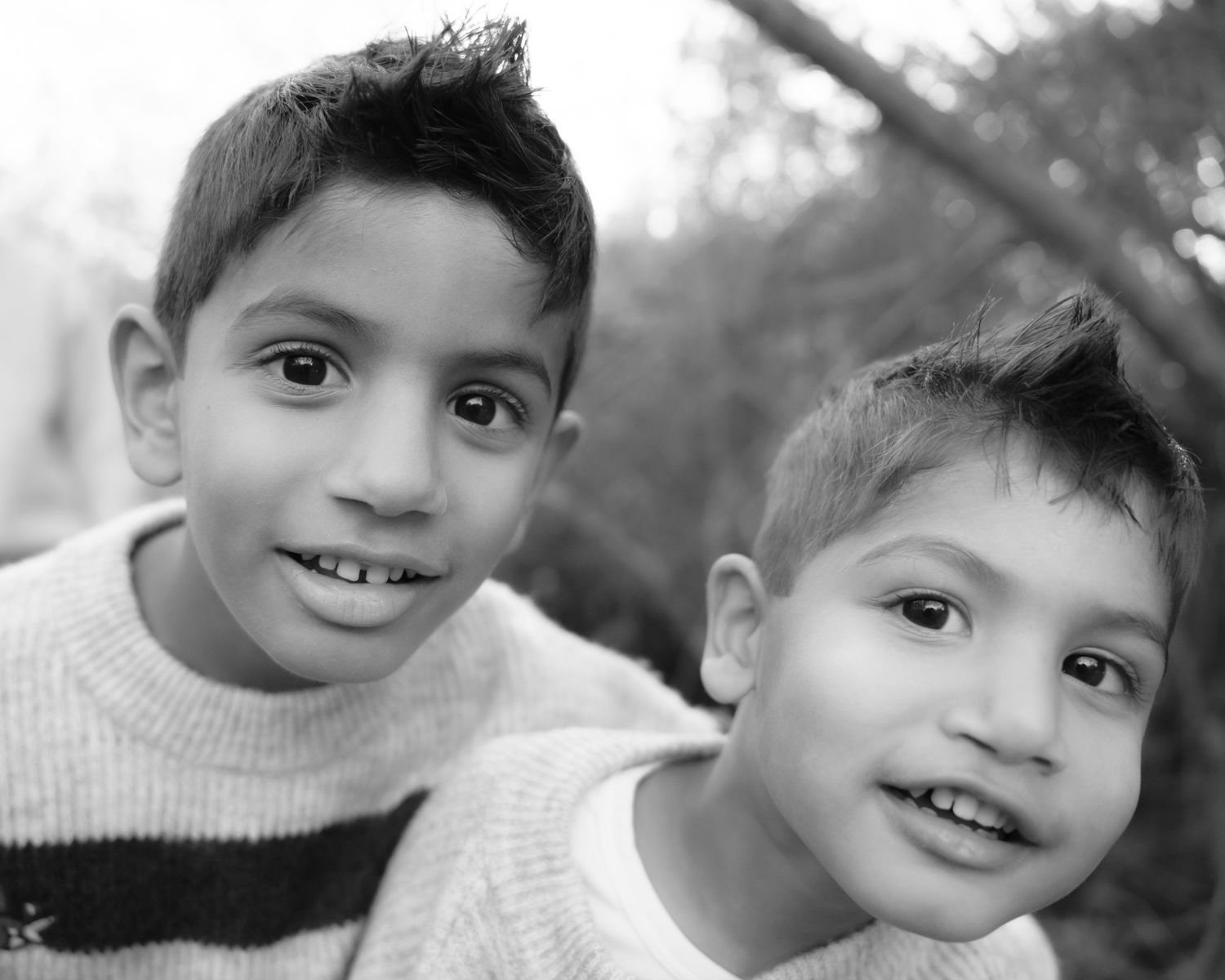Two young boys smiling at the camera in a black and white outdoor portrait photo.