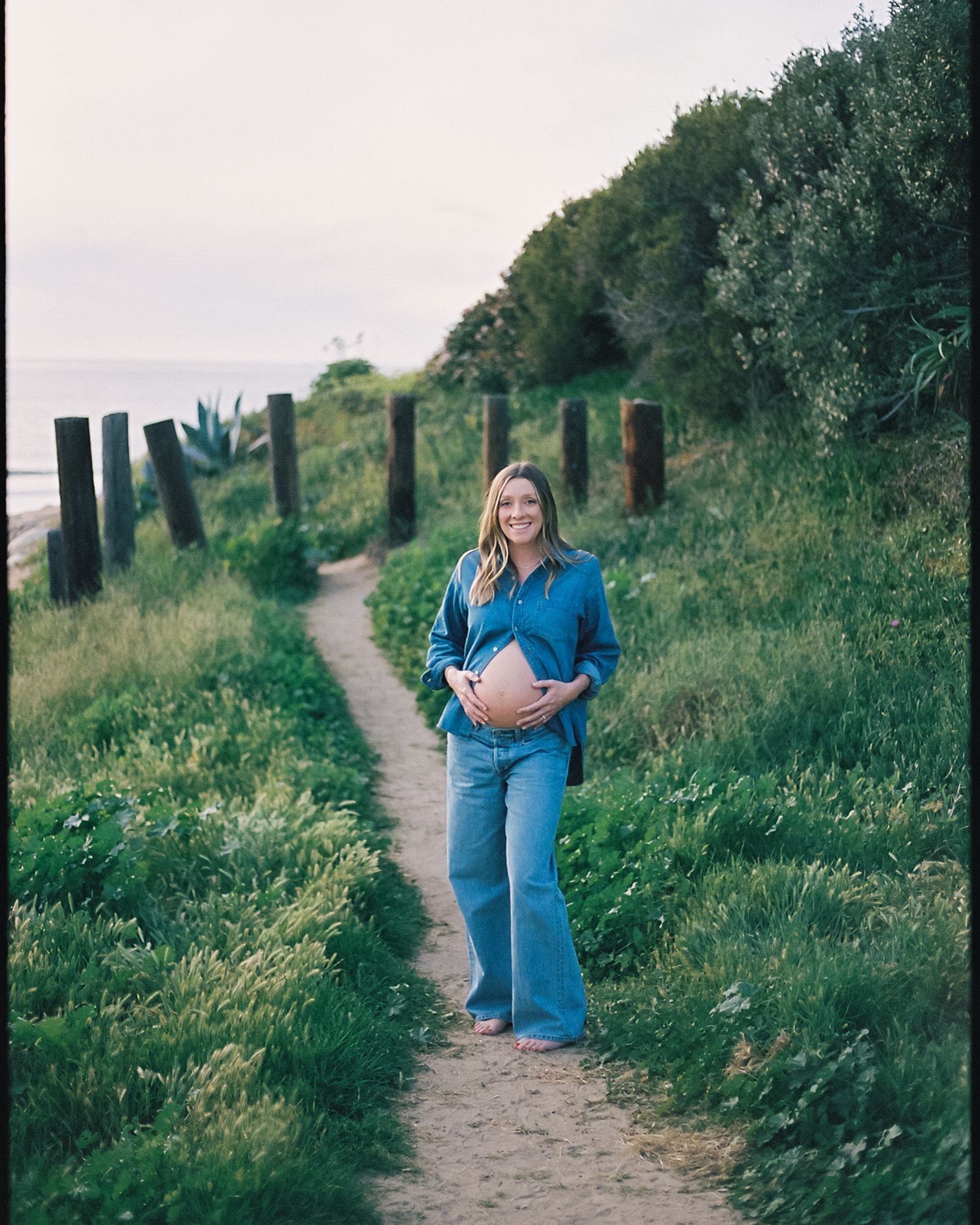 Two people embrace on a grassy hillside path during a romantic outdoor photo session.