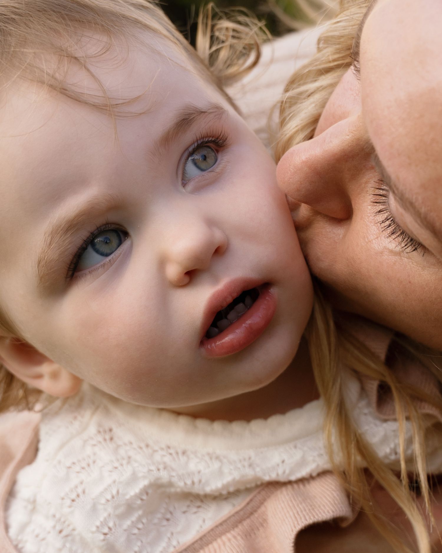 Close up of a tender moment between parent and child with blonde hair and bright blue eyes.