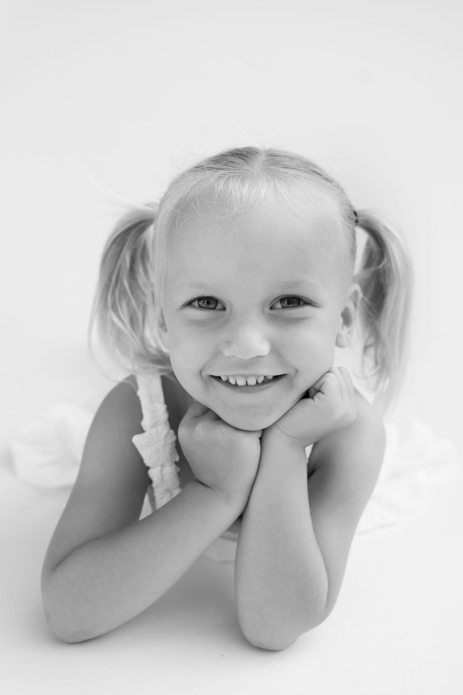 Black and white portrait of a smiling young girl with pigtails resting her chin on her hands.