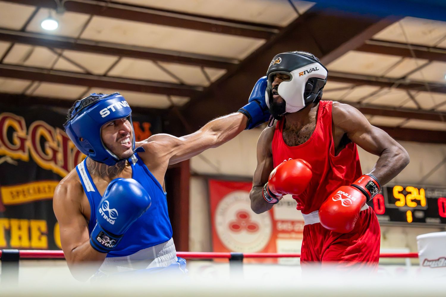 Two boxers compete in a ring, one in blue gear throwing a punch at opponent in red during an amateur boxing match.