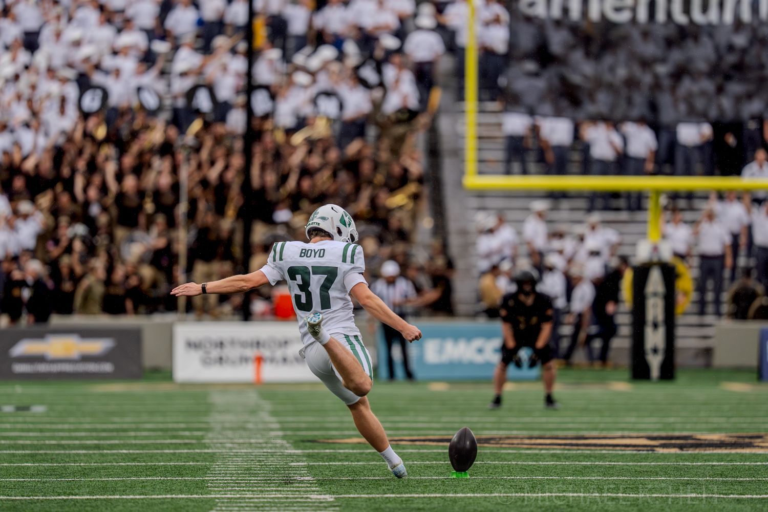 Football player attempts field goal kick during intense game at stadium.