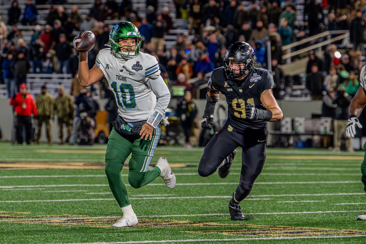 A player in green uniform runs with the ball while being pursued by a defender in black.