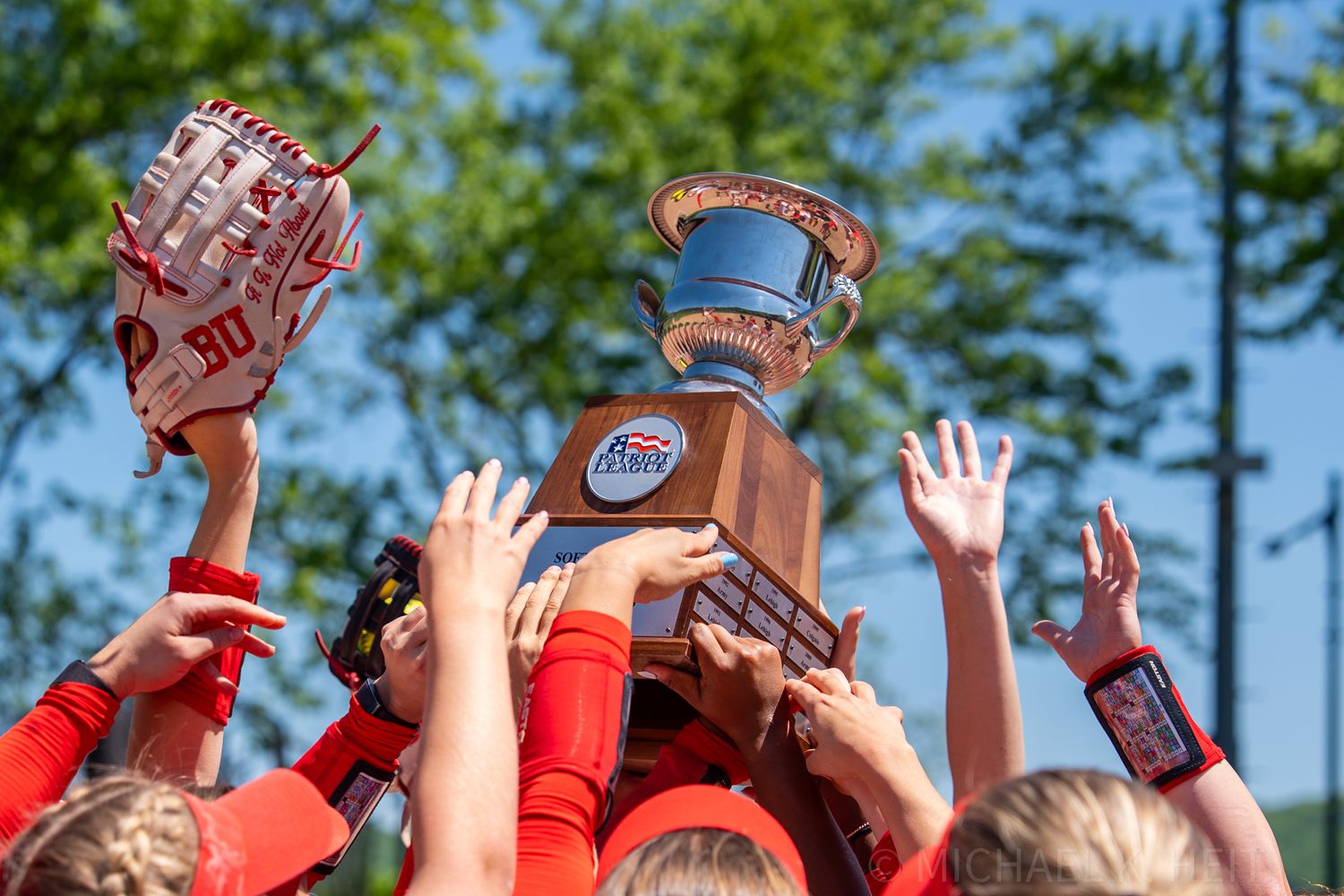 Team holding up championship trophy with raised hands against blue sky.