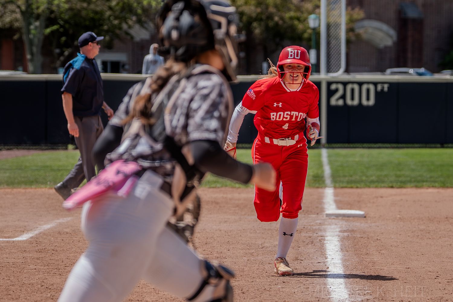 Softball player in red uniform runs toward home plate during game.