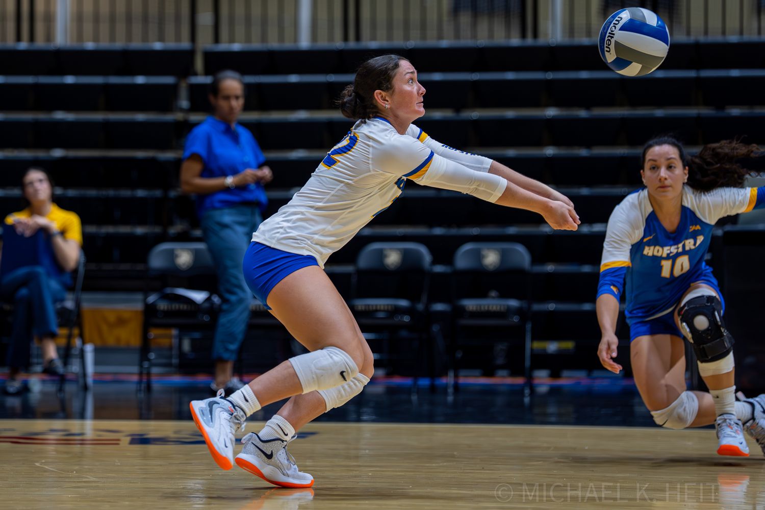 A volleyball player dives low to save the ball during a competitive indoor match.