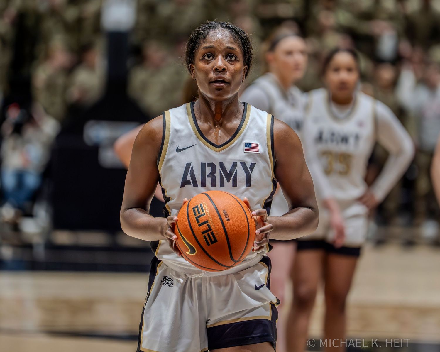 Basketball player in Army uniform holds the ball during a game against Navy at a crowded arena.