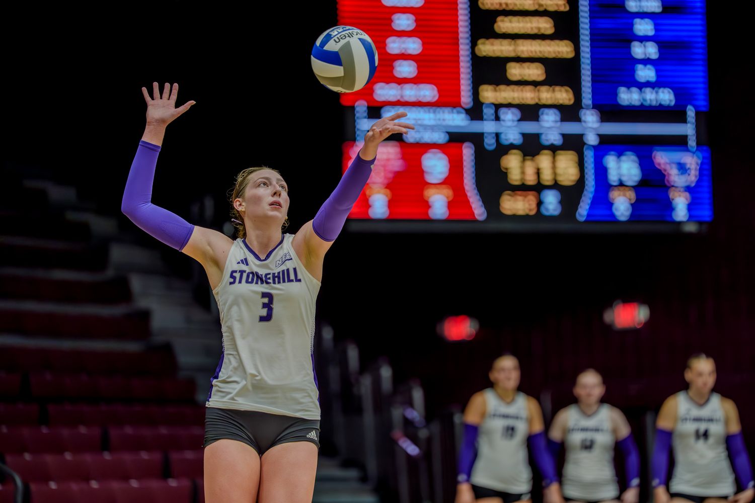 Volleyball players compete in an intense match with scoreboard visible in the background.