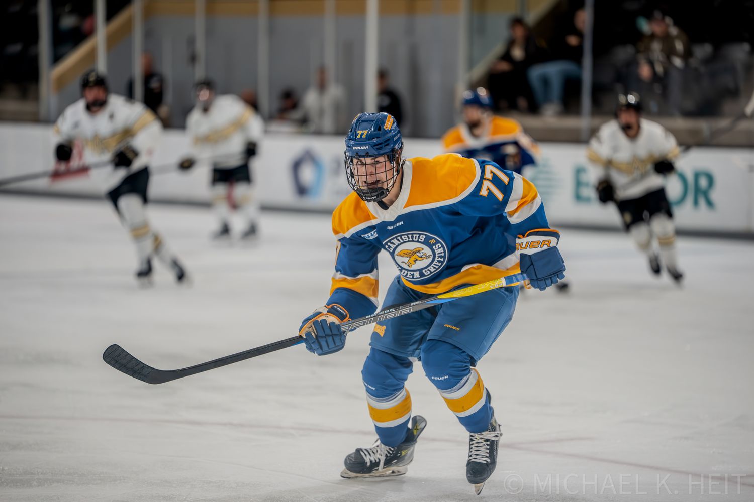 Hockey player in yellow and blue jersey skates aggressively across ice during game play.