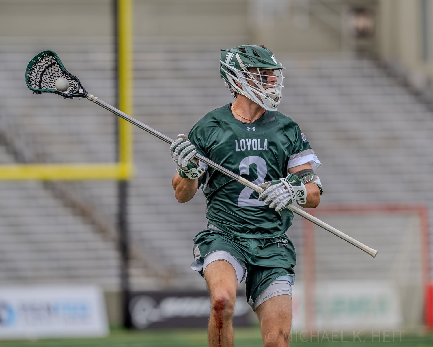 Two lacrosse players in green and white uniforms competing for the ball during a match.