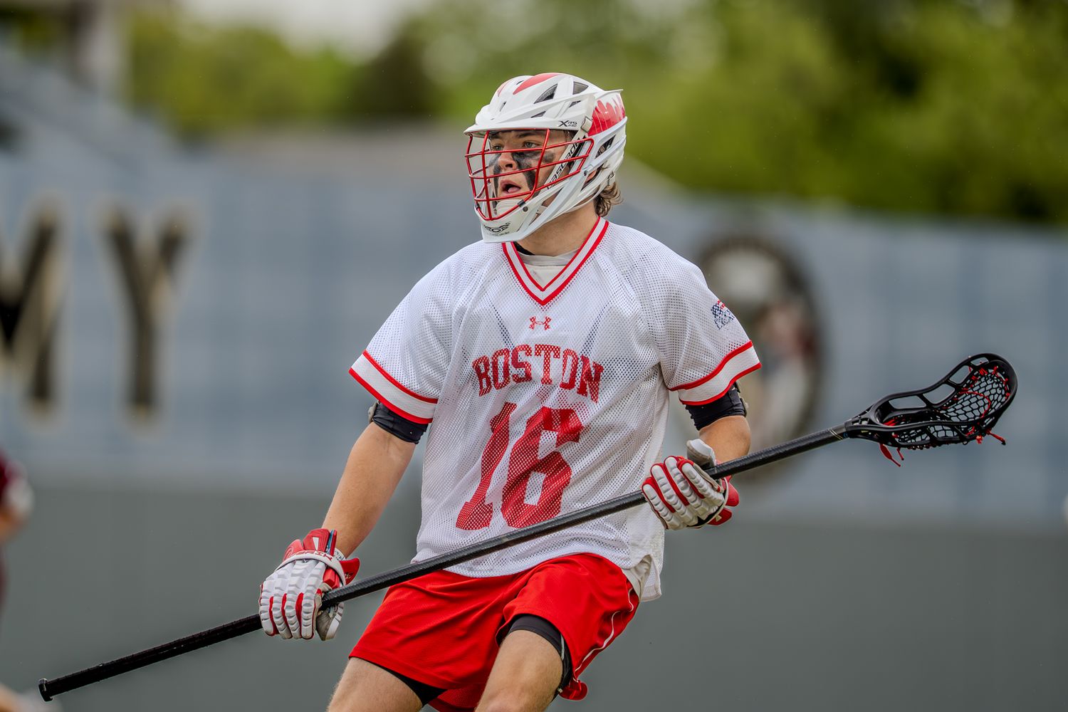 Boston University lacrosse player cradles the ball while running during gameplay.