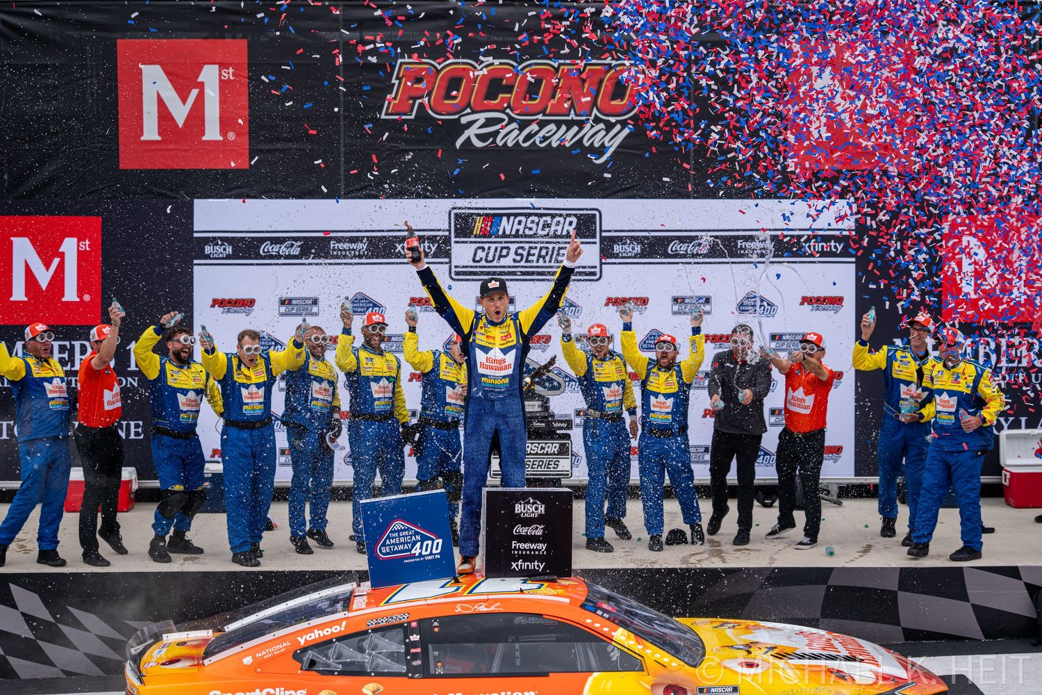 NASCAR Cup Series victory lane celebration at Pocono Raceway with winning team in blue uniforms and confetti.