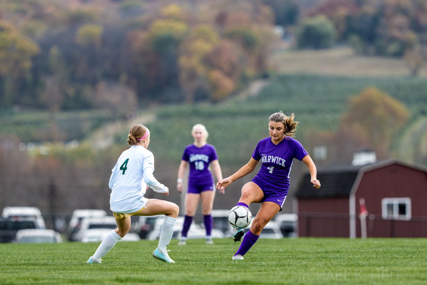 Soccer players slide tackle for possession of the ball during an intense match on a grass field.