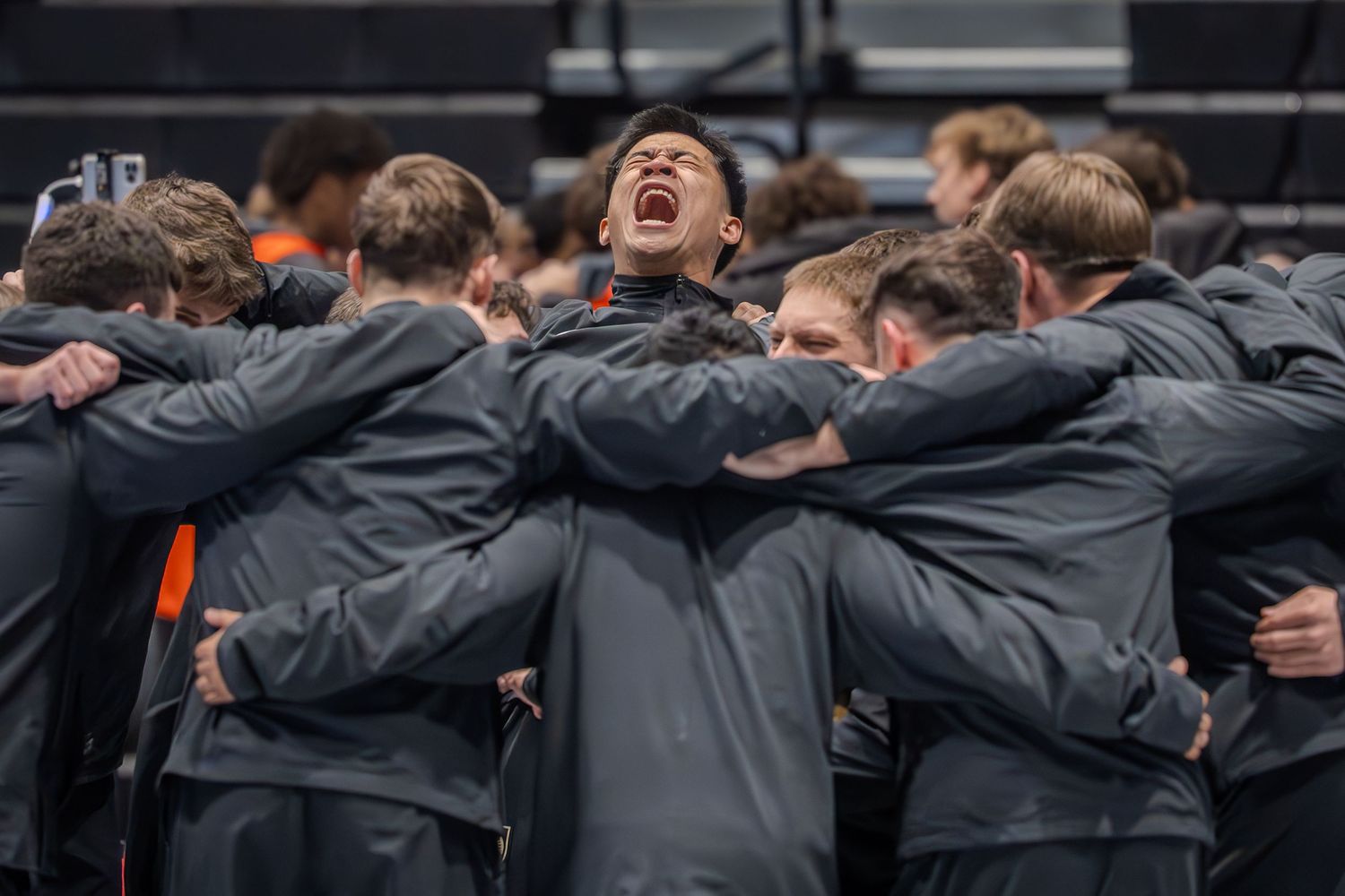 Athletes in gray jackets huddle together in an intense team meeting on a basketball court.