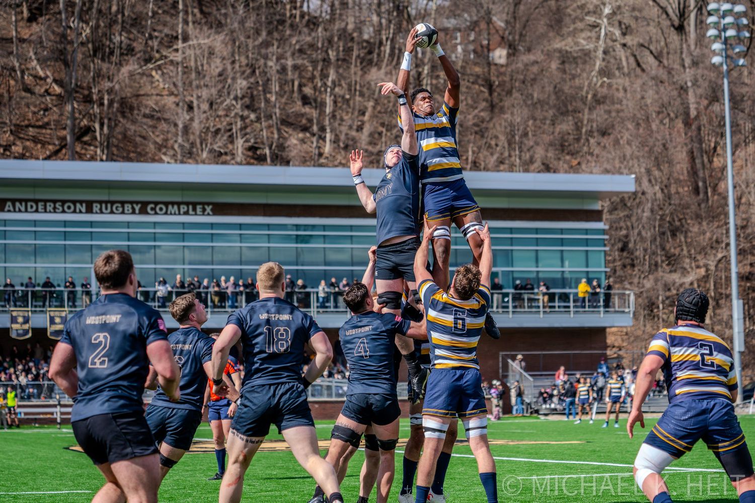 Rugby players engage in a scrum formation during an intense match on a green field with spectators watching.