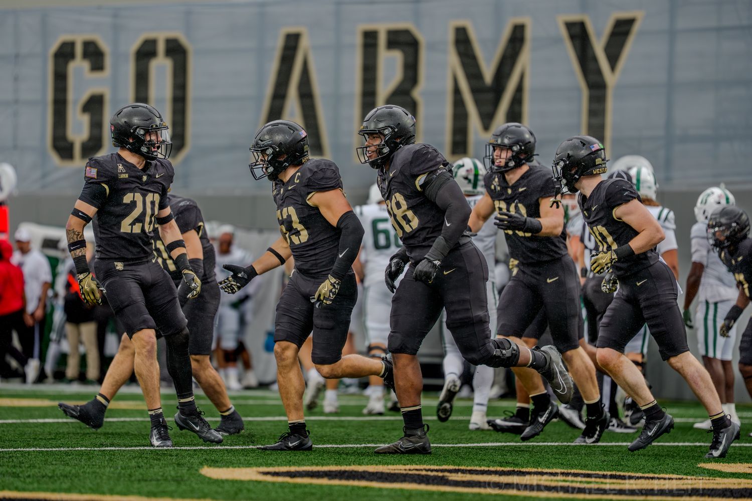 Army football players in black uniforms run drills during practice on the field.