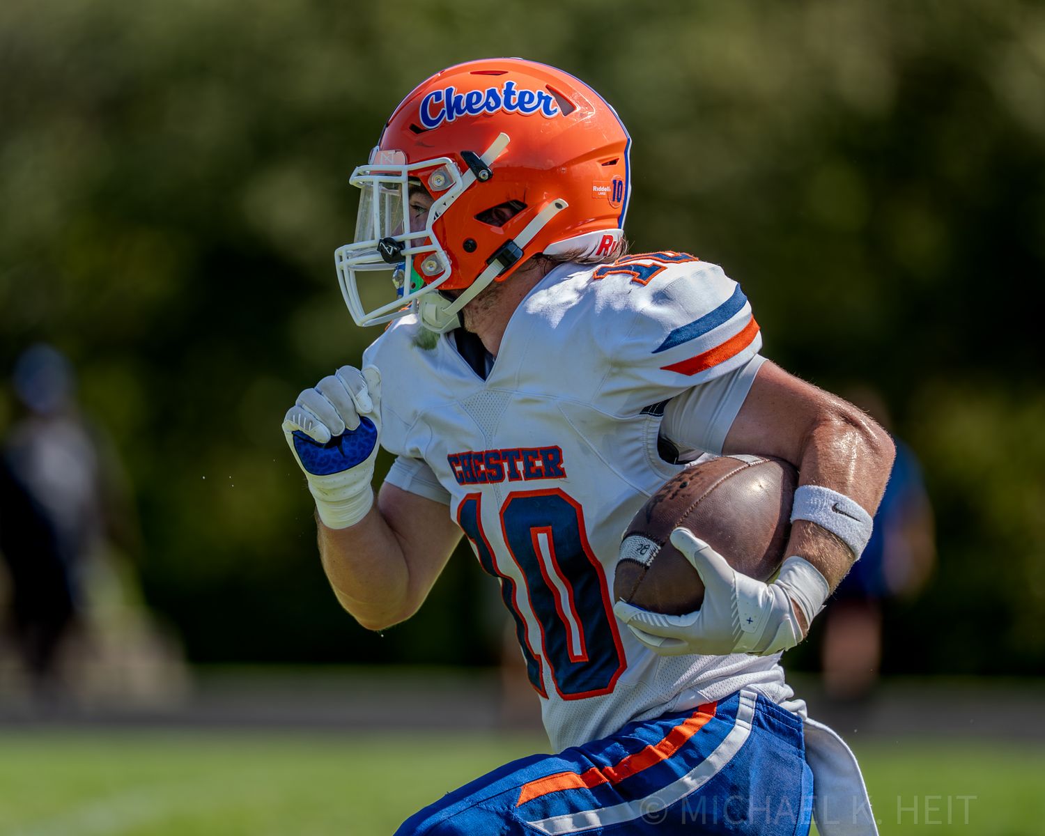 Football players in orange and blue uniforms run with the ball during a game.