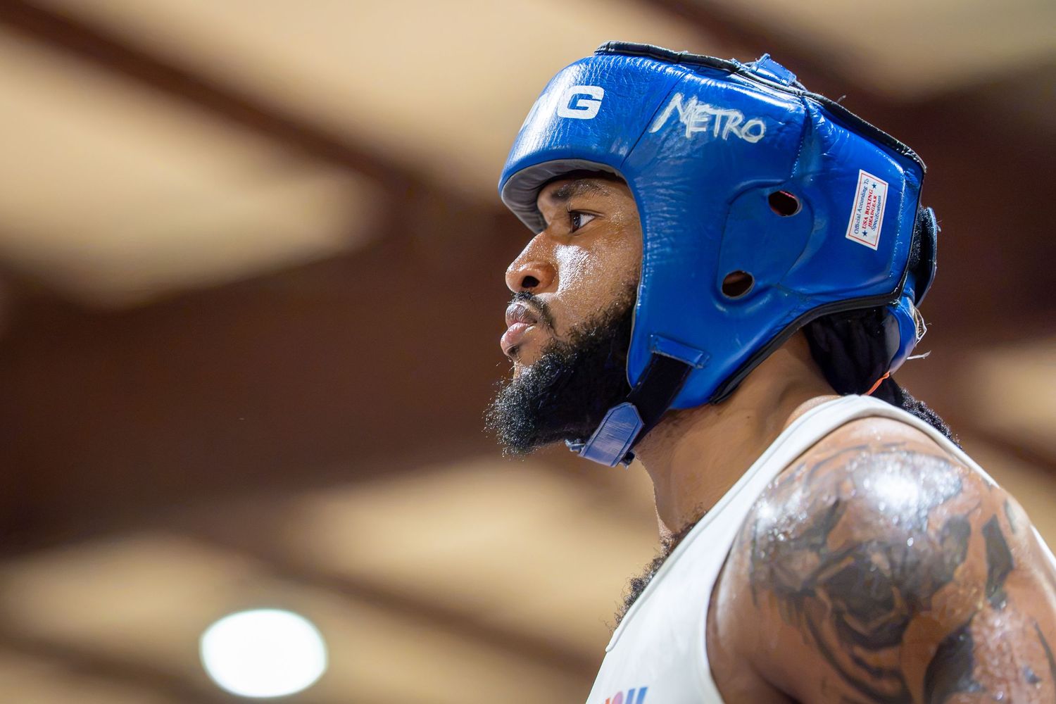 Boxer wearing blue Netro headgear looks upward during training session, showcasing tattoos on arm.