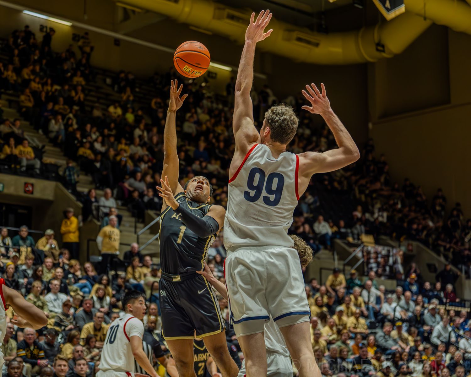Players leap high to contest a basketball shot during an intense game moment.