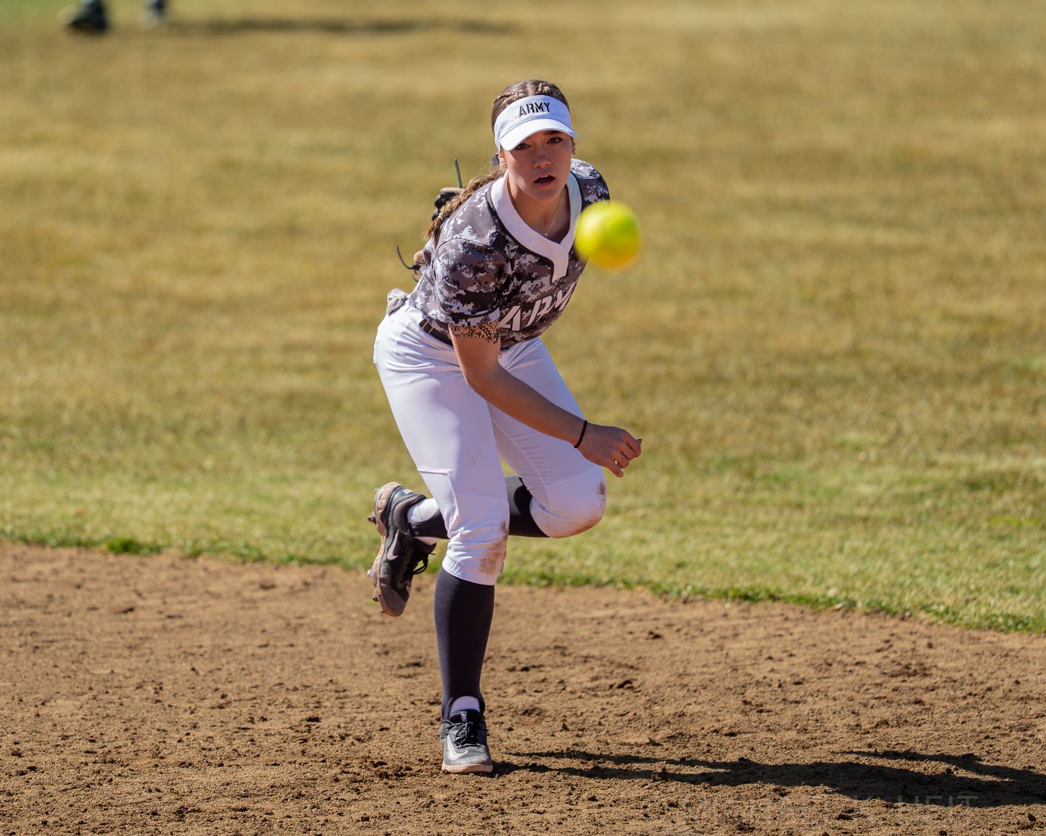 Softball pitcher in white uniform releases pitch during outdoor game.