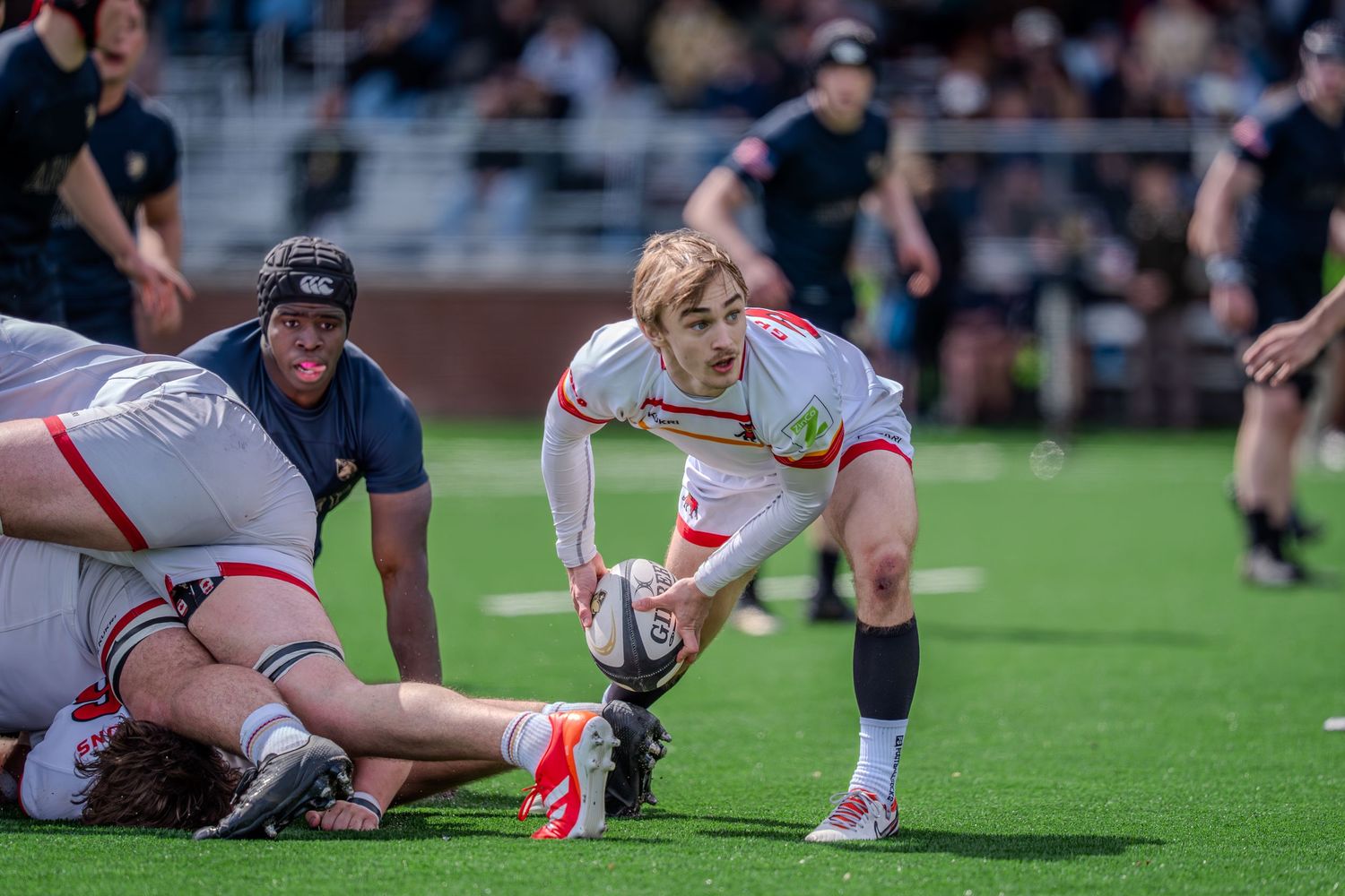 Rugby player reaches down to grab the ball during an intense match on the grass field.