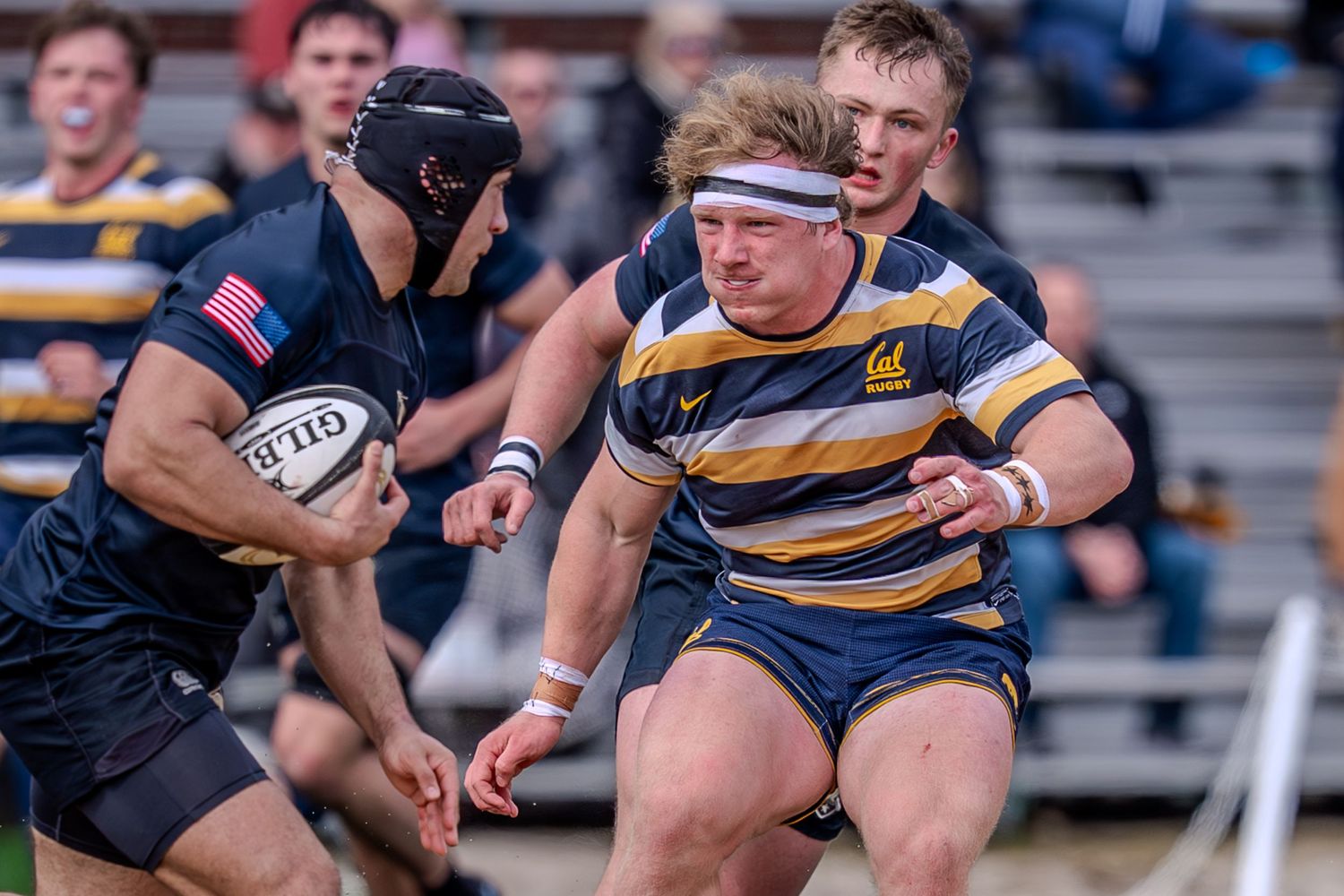 Rugby players compete for possession during an intense match between two teams in striped and dark uniforms.