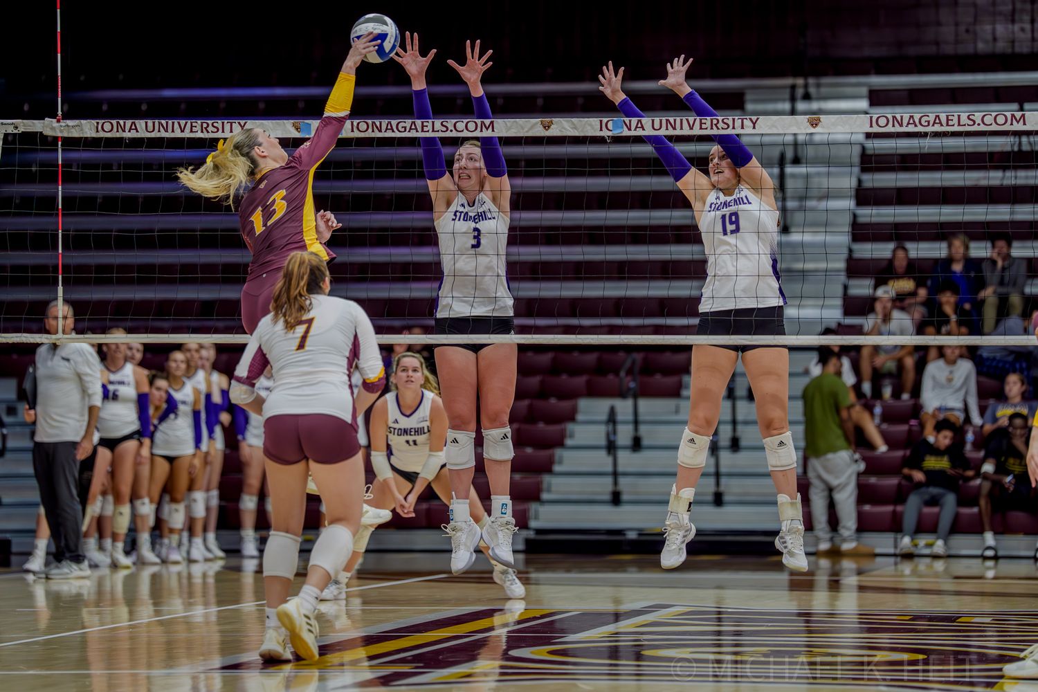 Volleyball players jump to contest the ball during a competitive indoor game.