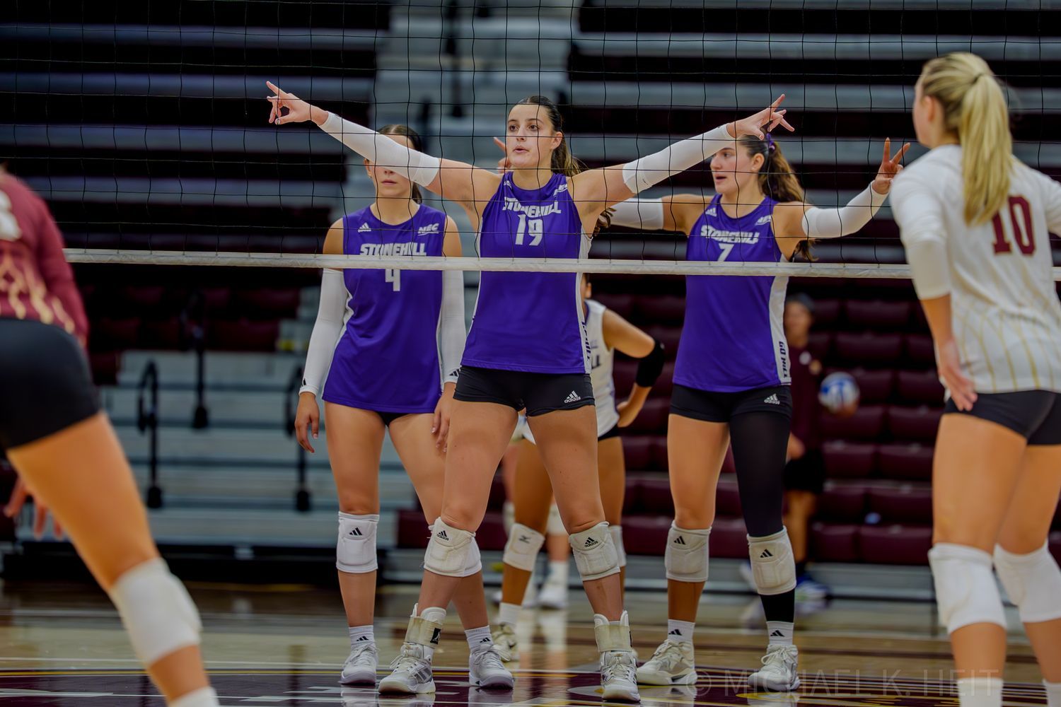 Volleyball players in purple jerseys signal and communicate during a game.